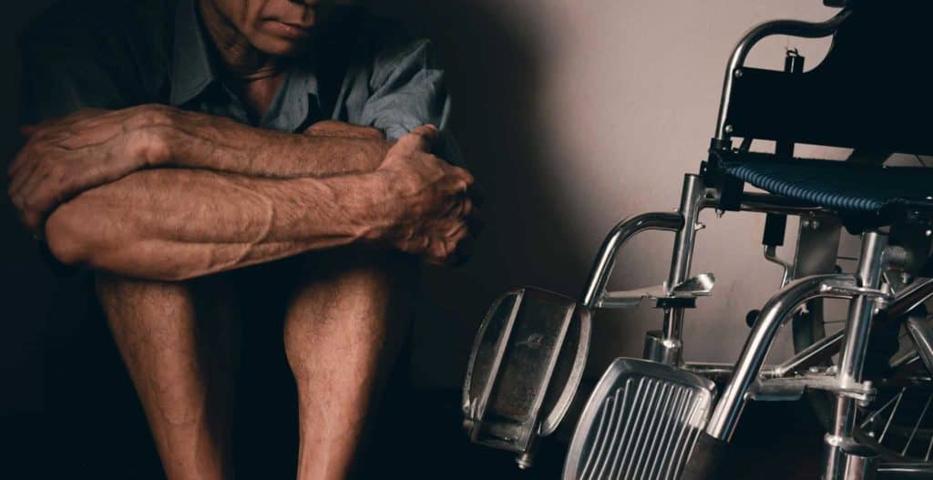 Distressed person sits in shadow next to a wheelchair.