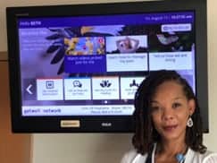 Patricia Sutton, Veteran Health Education Coordinator at Central Virginia VA Health Care System, stands in front of a GetWell Inpatient screen.