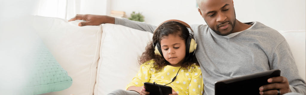 Man and child sit on couch looking at tablets
